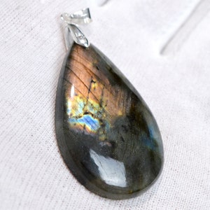 Peut inclure: Un pendentif en forme de larme en labradorite avec des reflets irisés bleus, verts et dorés. Le pendentif est monté sur une bélière en argent.