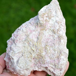 May include: A rough, irregularly shaped rock with a white and pink color. The rock has a rough, textured surface and appears to be made of a combination of minerals.
