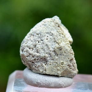 May include: A close-up of a white, rough, and textured rock with a light brown hue. The rock is sitting on a grey and pink surface.