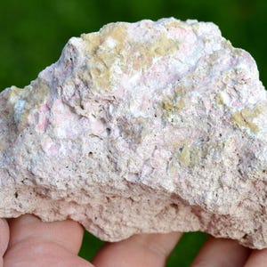May include: A rough, pink and beige rock with a porous texture. The rock has a natural, irregular shape.
