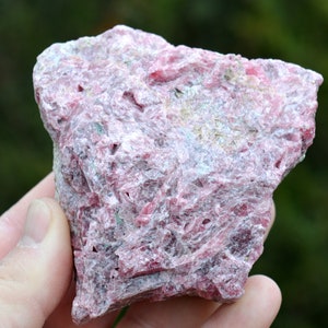 Puede incluir: Un gran cristal rosa y blanco áspero con una textura en capas y estriada. El cristal tiene un aspecto natural y bruto.