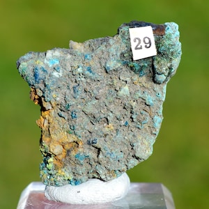 Può includere: Una roccia ruvida, grigia, verde e blu con un'etichetta bianca che dice "29".