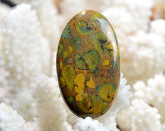 May include: Oval shaped green and yellow jasper cabochon with a brown matrix. The stone has a mottled pattern with green and yellow spots.