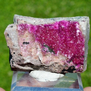 May include: A pink and white mineral specimen with a rough, textured surface. The mineral is a cluster of small, sparkly crystals.