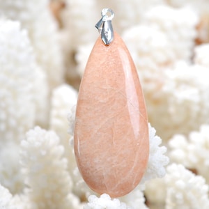 Può includere: Un ciondolo a forma di lacrima in pietra di sole rosa chiaro con un'anellina in argento.