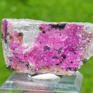 May include: A pink and white mineral specimen with a rough, textured surface. The mineral is a cluster of small, sparkly crystals.