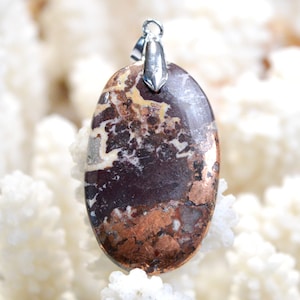 Peut inclure: Un pendentif ovale en cuivre et blanc avec une bélière en argent. Le pendentif a un motif marbré avec des paillettes de cuivre.