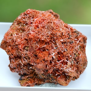 Könnte beinhalten: Ein Cluster aus roten, orangefarbenen und braunen Kristallen mit einer rauen, strukturierten Oberfläche. Die Kristalle sind in einer dichten, geschichteten Formation angeordnet, was ein visuell interessantes und einzigartiges Exemplar ergibt.