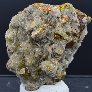 May include: A cluster of light brown, grey, and gold crystals with a rough, textured surface. The crystals are arranged in a random pattern and have a metallic sheen.
