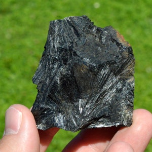 May include: A black, rough, and jagged rock with a crystalline structure. The rock has a silvery sheen and appears to be made of many small, sharp crystals.