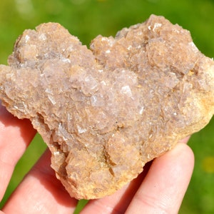 Puede incluir: Un cúmulo de cristales de fluorita de color marrón claro y rosa con una textura natural rugosa.