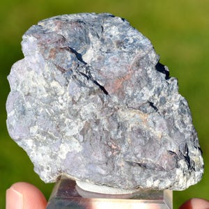 Può includere: Una roccia ruvida di colore grigio e viola con una texture cristallina. La roccia è circa delle dimensioni di un pugno e ha una forma naturale irregolare.