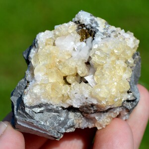 May include: A cluster of small, yellow calcite crystals on a dark gray matrix. The crystals are translucent and have a glassy luster. There are also some smaller, white crystals present.