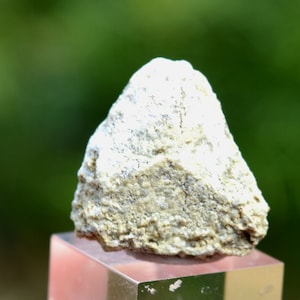 May include: A white, rough, irregularly shaped rock with a pointed top. The rock is sitting on a clear glass display stand.