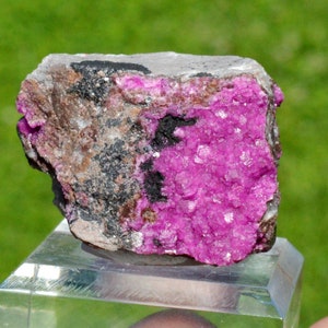 May include: A pink and grey mineral specimen with a rough, textured surface. The mineral is a cluster of small, sparkly crystals.