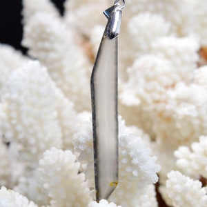 May include: A clear, grey, and white gemstone pendant with a silver bail. The pendant is shaped like a long, thin rectangle with rounded edges.