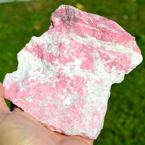 May include: A large, rough piece of pink and white striped gemstone. The stone has a natural, unpolished look.