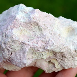 May include: A rough, porous rock with a pink and white color. The rock has a textured surface and appears to be a natural formation.