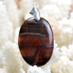 Peut inclure: Un pendentif en œil de tigre rouge avec une bélière en argent. La pierre a une couleur rouge foncé riche avec des rayures brunes et noires.