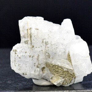 Peut inclure: Un groupe de cristaux de calcite blancs avec une couche de pyrite dorée au fond.