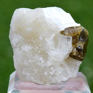 Puede incluir: Ejemplar mineral natural en bruto con una gran formación cristalina blanquecina y un grupo de cristales más pequeño de color verde oliva oscuro. Los cristales tienen una superficie rugosa y texturizada.