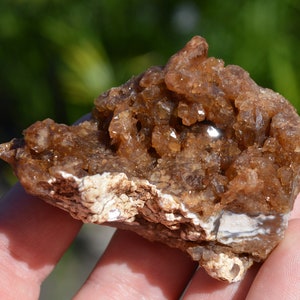 Könnte beinhalten: Ein Cluster aus braunen und weißen Kristallen auf einer rauen, natürlichen Gesteinsbasis. Die Kristalle sind durchscheinend und haben einen glasartigen Glanz.