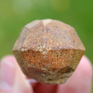 Puede incluir: Primer plano de una piedra preciosa de color marrón oscuro, facetada y con textura rugosa. La piedra preciosa tiene forma de dodecaedro.