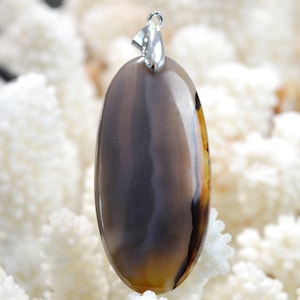Peut inclure: Un pendentif en agate brun et gris avec une bélière en argent. Le pendentif est de forme ovale et a une surface lisse et polie.