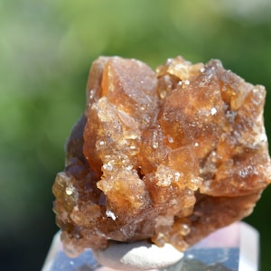 Könnte beinhalten: Ein Cluster aus braunen und orangefarbenen Kristallen mit einem glasartigen, durchscheinenden Aussehen. Die Kristalle sind in einem zufälligen, organischen Muster angeordnet, was ein einzigartiges und interessantes Display ergibt.