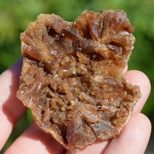 Könnte beinhalten: Ein Cluster aus braunen, durchscheinenden Kristallen mit einer rauen, strukturierten Oberfläche. Die Kristalle sind in einem zufälligen Muster angeordnet und haben ein natürliches, erdiges Aussehen.