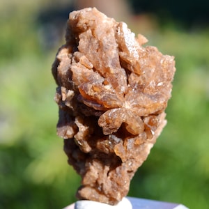 Könnte beinhalten: Ein Cluster aus braunen, durchscheinenden Kristallen mit einer rauen, strukturierten Oberfläche. Die Kristalle sind in einem radialen Muster angeordnet, was ein einzigartiges und auffälliges Display ergibt.