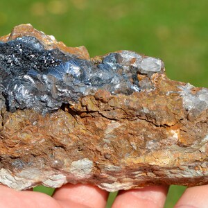May include: A close-up of a rock with a large, silvery-gray mineral deposit. The mineral has a layered, crystalline structure. The rock is brown and has a rough texture.