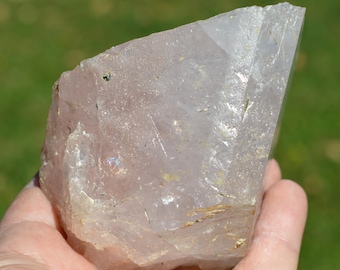 May include: A large, clear, pale pink crystal with a natural, rough surface. The crystal has a slight iridescent sheen and is partially translucent.