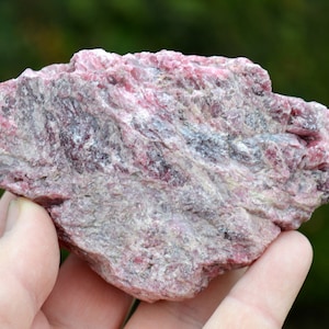 Puede incluir: Un gran espécimen mineral áspero, de color rosa y gris, con una textura estratificada y estriada.