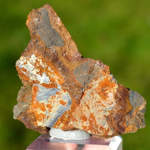 Puede incluir: Una roca rugosa de forma irregular con una mezcla de colores naranja, marrón, gris y negro. La roca tiene un aspecto estratificado con algunas áreas que muestran una estructura cristalina.
