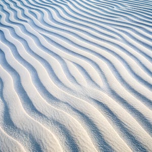 Può includere: Vista aerea di dune di sabbia bianca increspate con ombre morbide. L'immagine mostra un motivo di linee curve, creando un senso di consistenza e profondità. L'effetto complessivo è sereno e minimalista.
