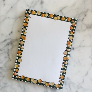 May include: A notepad with a black and white checkered border and a white interior. The border is decorated with orange slices.