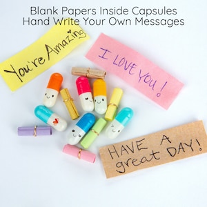 Pode incluir: C&aacute;psulas coloridas com rostos felizes cont&ecirc;m pap&eacute;is em branco para escrever mensagens. As c&aacute;psulas est&atilde;o espalhadas sobre uma superf&iacute;cie branca com notas adesivas coloridas que dizem "You're Amazing", "I Love You!" e "Have a great Day!"