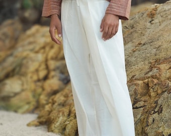 May include: A person wearing a rust-colored striped top with a white button closure and white wide-leg pants.