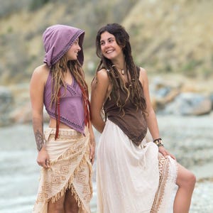 Può includere: Due donne che indossano abiti in stile bohémien. Una donna indossa un top halter viola con una gonna a motivi marroni e bianchi. L'altra donna indossa un top halter marrone con una gonna bianca con bordatura marrone. Entrambe le donne hanno i capelli lunghi e castani.