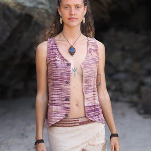 May include: A woman wearing a sleeveless, striped vest with a brown leather belt and a beige wrap skirt with fringe. She is wearing a blue stone pendant necklace and has a nose ring.