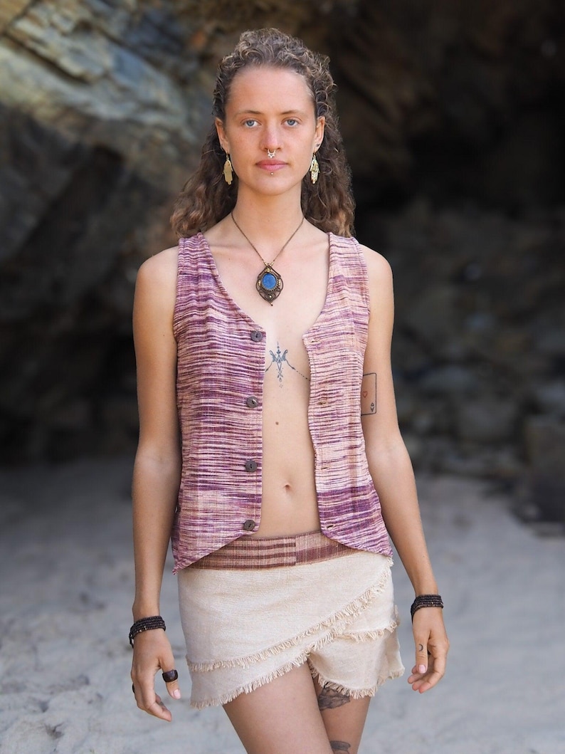 May include: A woman wearing a sleeveless, striped vest with a brown leather belt and a beige wrap skirt with fringe. She is wearing a blue stone pendant necklace and has a nose ring.