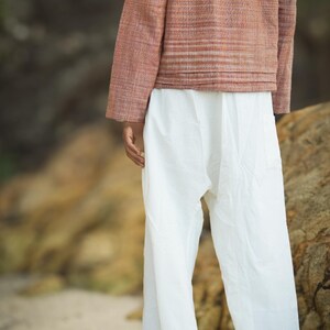 May include: A person wearing a long-sleeved, striped, rust-colored jacket with a hood and white pants.
