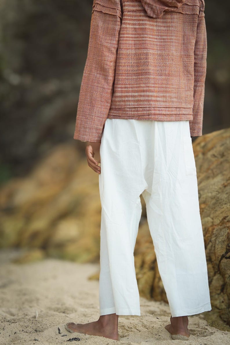 May include: A person wearing a long-sleeved, striped, rust-colored jacket with a hood and white pants.