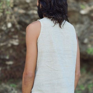 May include: A sleeveless, off-white linen top with a slightly asymmetrical hem. The top is made of a lightweight, breathable fabric and has a relaxed fit.