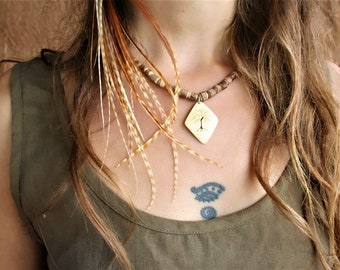 Könnte beinhalten: Eine Frau trägt ein grünes Tanktop mit einer braunen Perlenkette und einem goldenen Anhänger mit einem Baumdesign. Der Anhänger hängt an einer braunen Perlenkette. Die Frau hat lange braune Haare mit einer Federhaarextension.