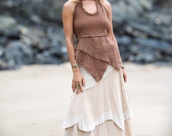 May include: A woman wearing a brown halter top with a frayed hem and a layered, cream-colored skirt with a frayed hem. The skirt has a flowing, tiered design. She is standing on a sandy beach.