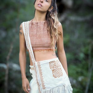 May include: A woman wearing a brown and white striped top with a white crocheted bag featuring a brown geometric design. The bag has a fringe trim.