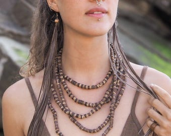 May include: A multi-strand necklace with brown and tan wooden beads. The necklace is layered, with each strand slightly longer than the one above. The beads are rectangular and strung together. The necklace is worn with a brown top.