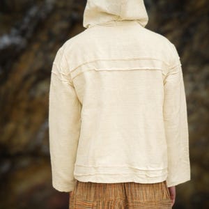 May include: A cream-colored hooded sweatshirt with long sleeves and a relaxed fit. The sweatshirt has a simple design with a single seam down the back.